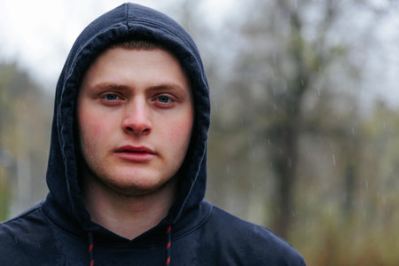 Portrait of a Young Adult Male with a Striking Gaze in Rainy Weather. A young mans portrait captures his chiseled jawline and strong features against an outdoor setting.の写真素材