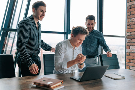 Successful group of young male colleagues working with laptops in the office. Three delighted coworkers using laptops and collaborating at workの写真素材