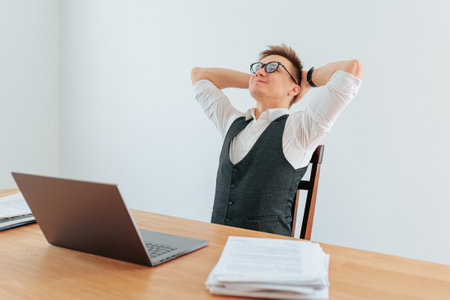 A white collar worker sitting alone in his office, smiling with satisfaction as he completes his daily tasks on his laptop. He is wearing a light blue shirt and a grey suit,の写真素材