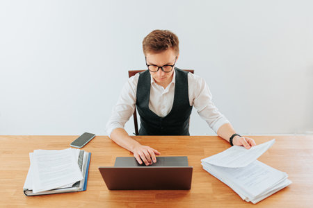 A white-collar office worker in his home office, wearing glasses and a dress shirt, looks intently at his laptop screen, typing rapidly as he works on a project.の写真素材