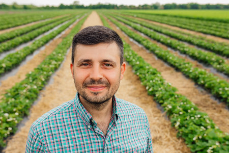 young bearded farmer of European nationality looks at the camera and smiles. male farmer dressed in shirt with squares is in the agricultural fieldの写真素材