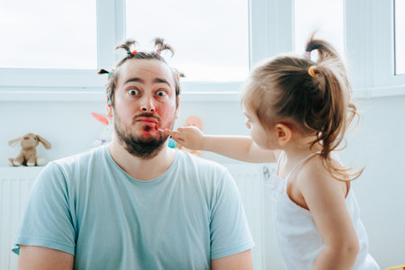 A dad and daughter sharing a fun and bonding moment while doing makeup together, creating funny and unique looks. Like Father, Like Daughter A Funny Family Moment Putting on Makeupの写真素材