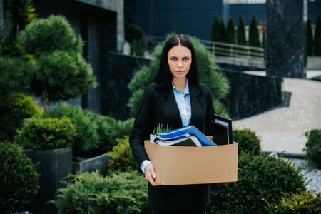 A woman outside with a box, feeling disappointed and jobless after losing her job. Jobless and Alone Woman Holding Box of Belongingsの写真素材