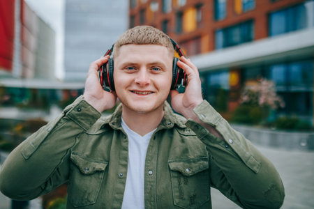 A young man with headphones on, looking up at the city skyline and smiling as he listens to his favorite music. Building Bops Handsome Guy Relaxing with Headphones Onの写真素材