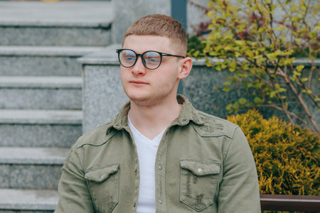 A portrait of a handsome young caucasian guy wearing stylish eyeglasses and exuding a graceful and youthful charm while enjoying the beautiful outdoor scenery.の写真素材