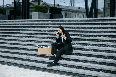 A troubled woman talking on the phone and holding a mobile phone after being fired from her job.の写真素材