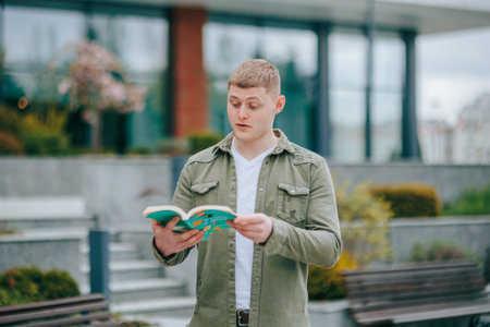 A young man reading a book in the park, gazing off into the distance with a look of wonder and amazement. Exploring the Pages A Young Male Surprised by the Knowledge in His Bookの写真素材