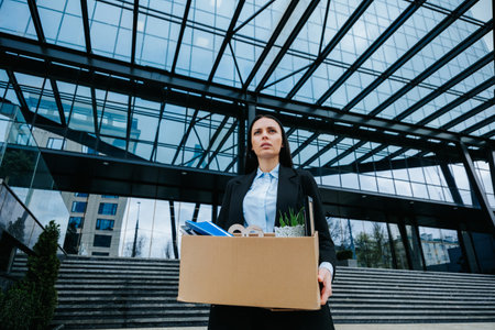 Feeling the Effects of Job Loss A Struggle to Make Ends Meet. A woman in a white collar holds a cardboard box, her expression reflecting the stress of workloss and unemployment.の写真素材
