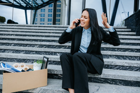 A woman who is unemployed and feeling troubled while talking on the phone with her smartphone while sitting on the stairs outside, Emotional Conversation Woman on Mobile Phoneの写真素材