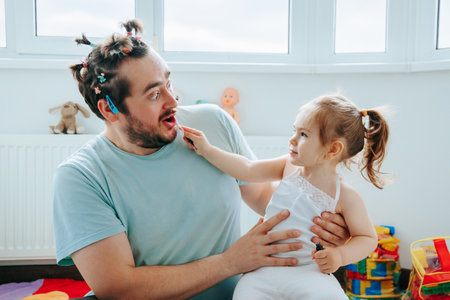 A family bonding over a silly and entertaining makeup session, with the father and daughter creating funny looks and making memories. Price of Beauty A Dad and His Daughter Share a Funny Momentの写真素材
