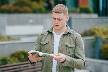 A male student studying on campus, completely focused and amazed by the textbook in front of him. Natures Classroom A Young Man Stunned by the Beauty of His Surroundings While Readingの写真素材