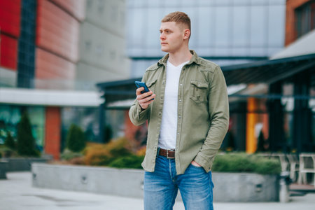 Charming boy with a mobile phone. Young male with mobile phone exploring city on his own. Content boy relaxing with his smartphone in the cityの写真素材