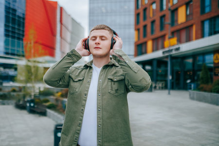 A man wearing a red shirt and headphones, looking at the cityscape while enjoying his music. City Soundtrack Handsome Man with Headphones On Listening to Musicの写真素材