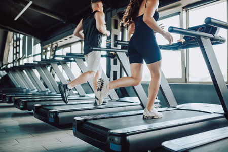 Hispanic and American Couple run treadmill Fitness in the Gym. Caucasian Man and Hispanic Woman Engaged in Intense Workout. Young Fit Couple Training Together at the Gymの写真素材