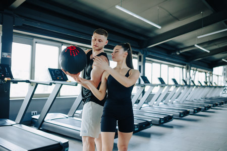 A hispanic woman, under the guidance of her personal trainer, participating in a challenging workout routine with a training ball, aimed at improving her strength and endurance.の写真素材