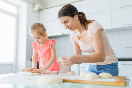 Embracing domestic creativity, a young mom and her daughter prepare dough in the kitchen, nurturing family connections. Wholesome Family Moments Mother and Daughter Prepare Dough at Homeの写真素材