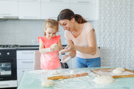 The kitchen becomes a hub of family joy as a mother and daughter prepare dough together, savoring every moment. Domestic Harmony Mother and Daughters Joyful Kitchen Dough Preparationsの写真素材