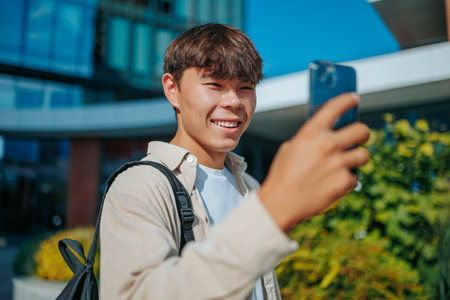 A portrait of a happy young man talking on his mobile phone in an outdoor setting. Korean Students Portrait Satisfied in Smartphone Conversationの写真素材