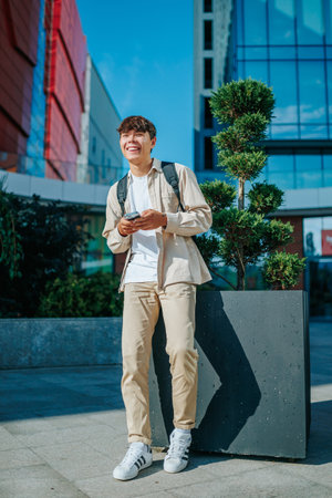 An outdoor conversation between a happy student and a friend, both using smartphones. Real People, Real Conversations Outdoor Smartphone Chatの写真素材