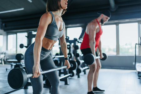 A pair of fitness enthusiasts, an American male and a Hispanic female, exhibit their muscular prowess while lifting weights during their workout.の写真素材