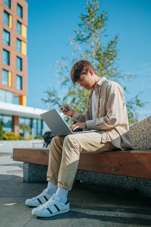 A motivated, young Asian Korean student, balancing work and education, immersing himself in laptop studies while surrounded by the invigorating atmosphere of the outdoors.の写真素材
