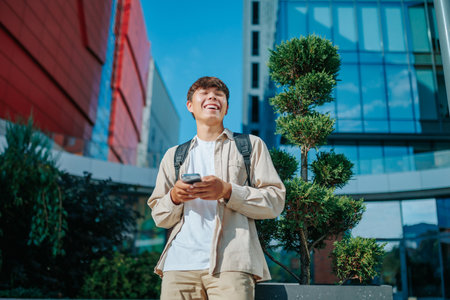 A joyful teenage boy engrossed in a chat with friends on his mobile phone. The Joy of Connection Smiling Student in Dialogueの写真素材
