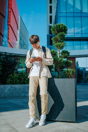 Satisfied Korean Student, Smiling in Online Conversation on Smartphone, Embraces the Outdoors. Outdoor Online Dialogue Asian Student Smilingの写真素材