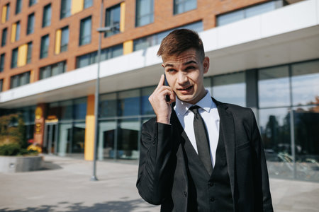 A young Caucasian American man, dressed in a sharp business suit, expresses his anger while engaged in a heated phone conversation on the bustling streets of the urban district.の写真素材