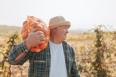 Enter a rural plantation where an industrious man tends to the crops, embracing a bag filled with freshly harvested onions. Its a glimpse into the timeless connection between the landの写真素材