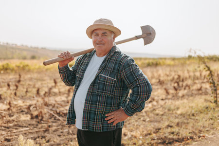 Rural Charm A Caucasian Farmer looking at camera Strolls through the Countryside, Shovel on His Shoulder, Embracing the Simplicity of Life. Tilling the Soil Senior Farmer with Shovel in Handの写真素材