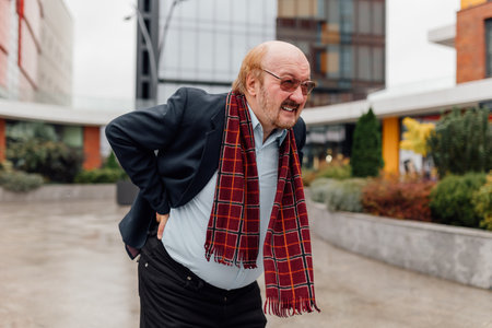 Of an elder senior bearded man and an upset old middle-aged grandfather, both stricken with sudden, intense back pain linked to rheumatism. The troubled individuals, outdoorの写真素材