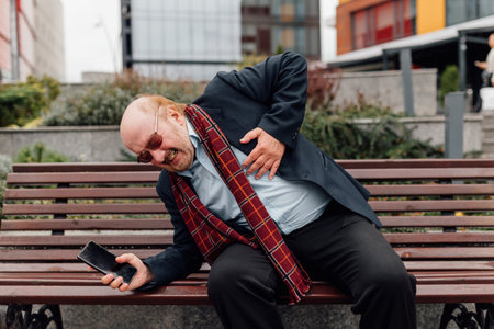 City Heart Crisis Upset senior bearded man calls for emergency aid, touched by sudden chest pain, possibly signaling a heart attack in an outdoor setting.の写真素材