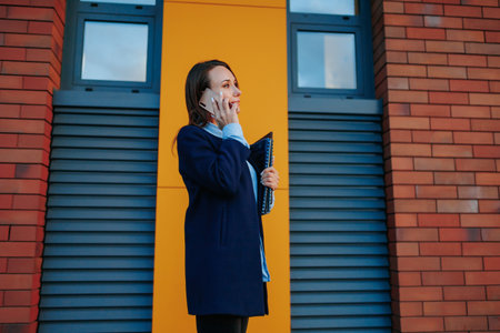 Corporate Dilemma A Puzzled American Businesswoman Walks and Talks on Her Smartphone, Balancing the Challenges of Work in a Modern Urban Setting.の写真素材