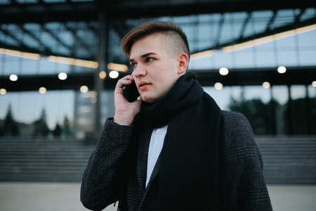 Casually confident businessman using his mobile phone outdoors, seamlessly blending technology and urbanity for a dynamic portrayal of contemporary work life.の写真素材