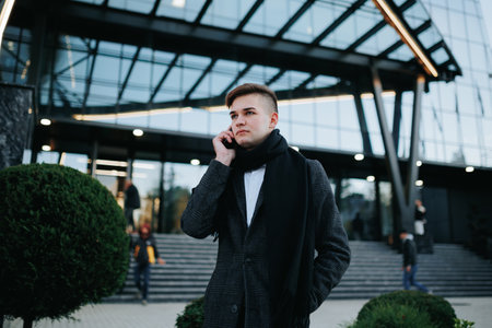 Confident young businessman engrossed in his smartphone, navigating city life with style and professionalism in a sleek modern setting.の写真素材