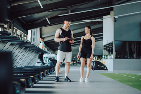 highlights the valuable guidance provided by a male personal trainer to a female client, as they engage in a detailed discussion about fitness goals, training strategies,の写真素材