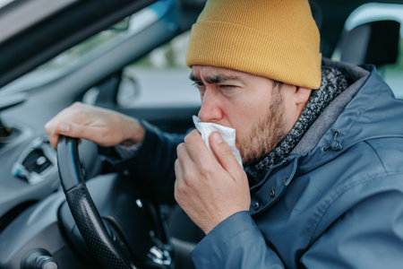 Experience the realities of flu season with a bearded chauffeur in this powerful image. The driver sneezes and coughs, highlighting the impact of seasonal illness on daily routines.の写真素材