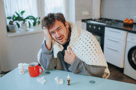 Immerse yourself in the nuanced reality of this photo, where a bearded man manages a headache and the flu while nestled in a comforting duvet at home. It captures the essence of grapplingの写真素材