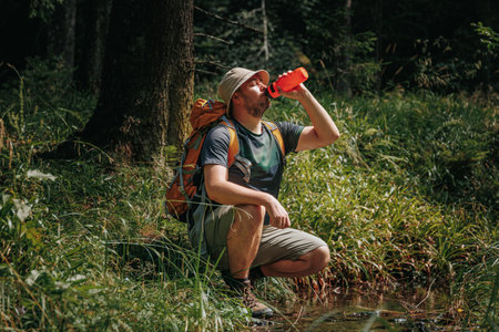 Witness the active lifestyle of an American guy, immersed in the journey of a hiking expedition, taking a pause in a wooded setting to drink water and revitalize for the trip ahead.の写真素材