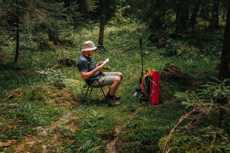 Discover the allure of literature in the heart of nature as a young Caucasian hiker, nestled in a wooded oasis, engages in the enchanting act of reading. With a book in hand and a backpack nearby,の写真素材