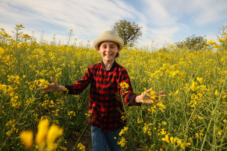 front view of a joyful kid children with hat Running with arms outstretched in sunny day. Charming little girl in a blooming rapeseed fieldの写真素材