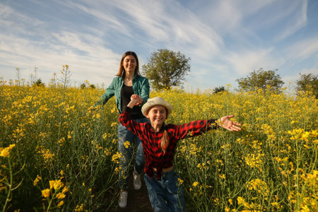 happy farmer family joyful run. happy family mom and fun little girl child summer kid dream concept. run through the yellow grass through the field at sunset in a slow paceの写真素材