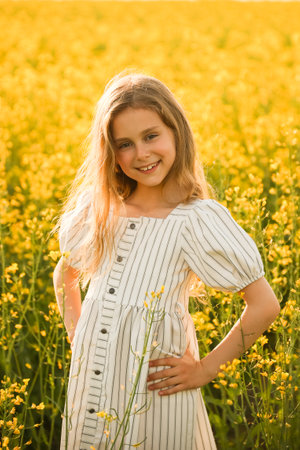 portrait of a gorgeous happy little kid girl in the dress, looking at camera. on a natural yellow background with flowering rapeseed. rustic, spring outsideの写真素材