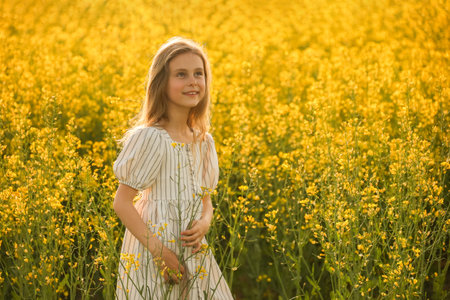 portrait of a beautiful happiness little kid girl in the dress, on a natural yellow background with flowering rapeseed. rustic, copy spaceの写真素材