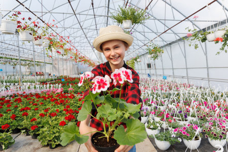smiling american kid with a potted plant flower in his hands. laughing child in greenhouse, happy childhood with many flowers, Copy spaceの写真素材