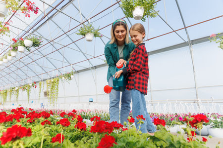 Mother florist and her little daughter work in the garden watering plants and flowers together in the summer. Watering plants. Little girl helps florist to water some flowers.の写真素材