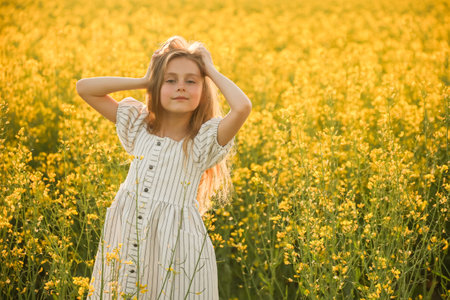 portrait of a pretty smiling little child girl in dress, looking at camera. on a natural yellow background with flowering rapeseed. rustic, rural contryの写真素材