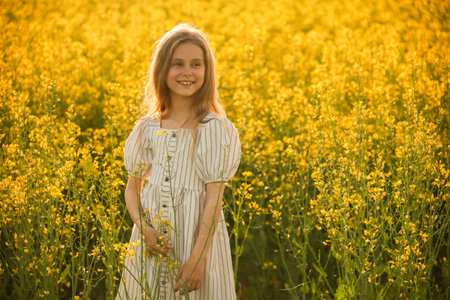 artistic portrait of a nice laughing little kid girl in the dress, the meadow in spring day with flowering rapeseed. rustic, fine artの写真素材