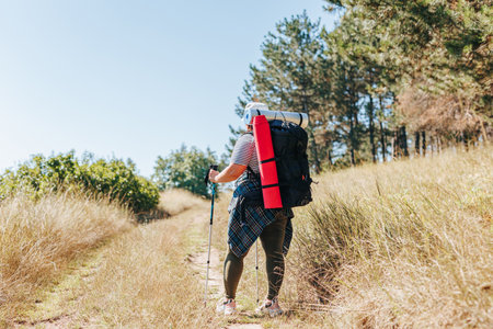 Embark on a visual adventure with this stunning shot of an overweight female hiker, as she walks alone through nature, showcasing the back view and the beauty of a healthy lifestyle.の写真素材