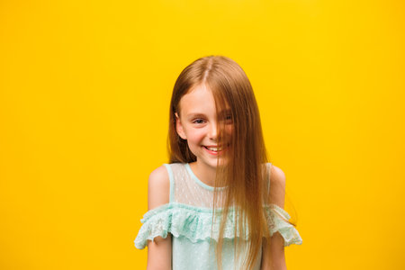 kid quite smiling happily, with blond hair, looking with satisfaction in front of the camera, being happy. the look in front of a beautiful child on the yellow background of the studio.の写真素材